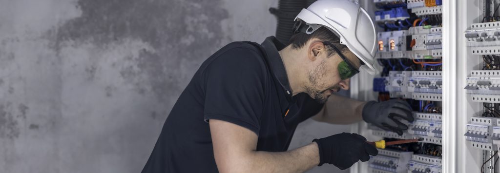 A male electrician works in a switchboard using an electrical connection cable.